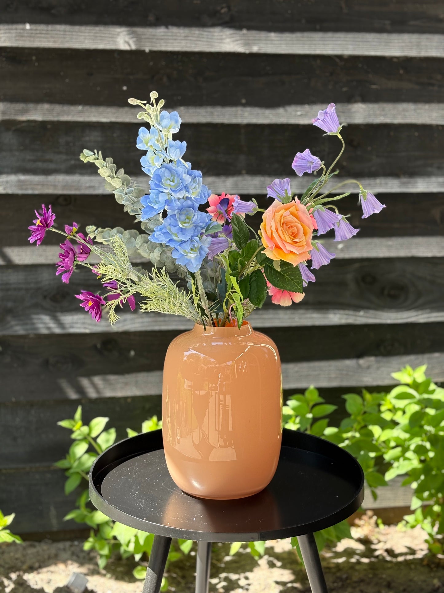 Sfeerfoto van zijden plukboeket van kunstbloemen met perzikkleurige roos, blauwe delphinium, roze en paarse cosmos