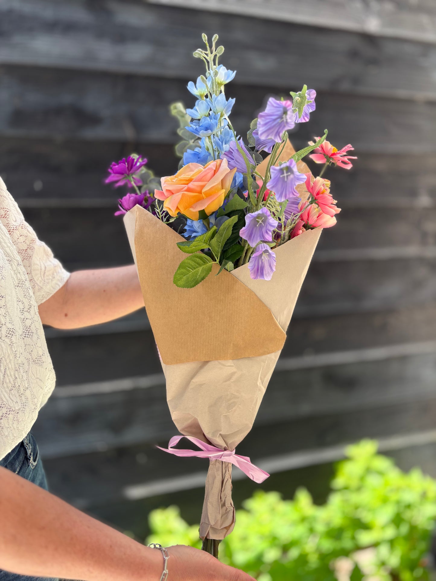 Zijden plukboeket van kunstbloemen met perzikkleurige roos, blauwe delphinium, roze en paarse cosmos zonder vaas