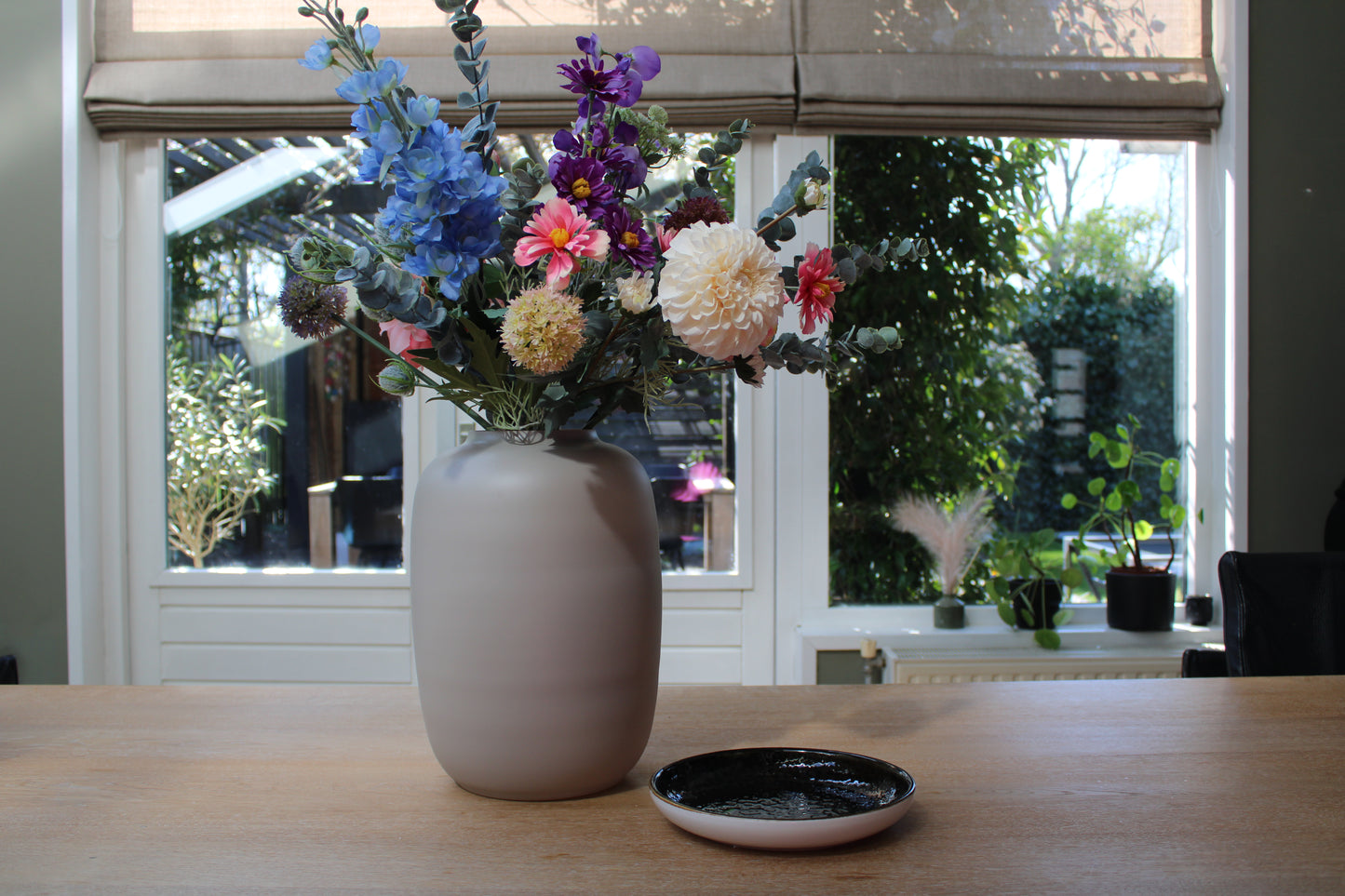 Zijden plukboeket met roze, paarse, blauwe, witte bloemen in ivoor kleurige vaas op een houten tafel