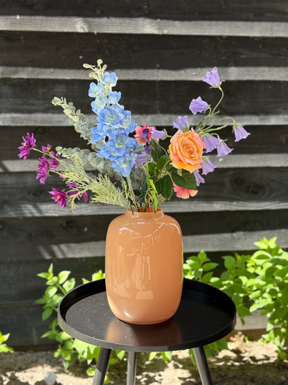 Sfeerfoto van zijden plukboeket van kunstbloemen met perzikkleurige roos, blauwe delphinium, roze en paarse cosmos