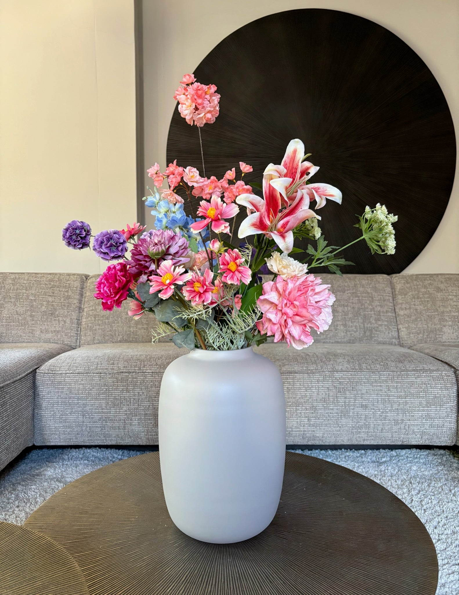 Zijden boeket Fleur met bonte kleuren, roze, paars, blauw in een ivoorkleurige vaas op een tafel