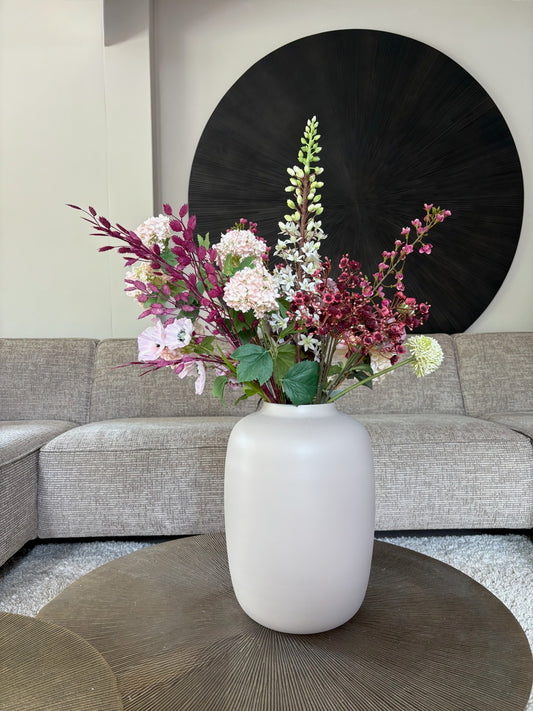 Zijden boeket Lily met paars en roze tinten in de ivoorkleurige vaas op een tafel
