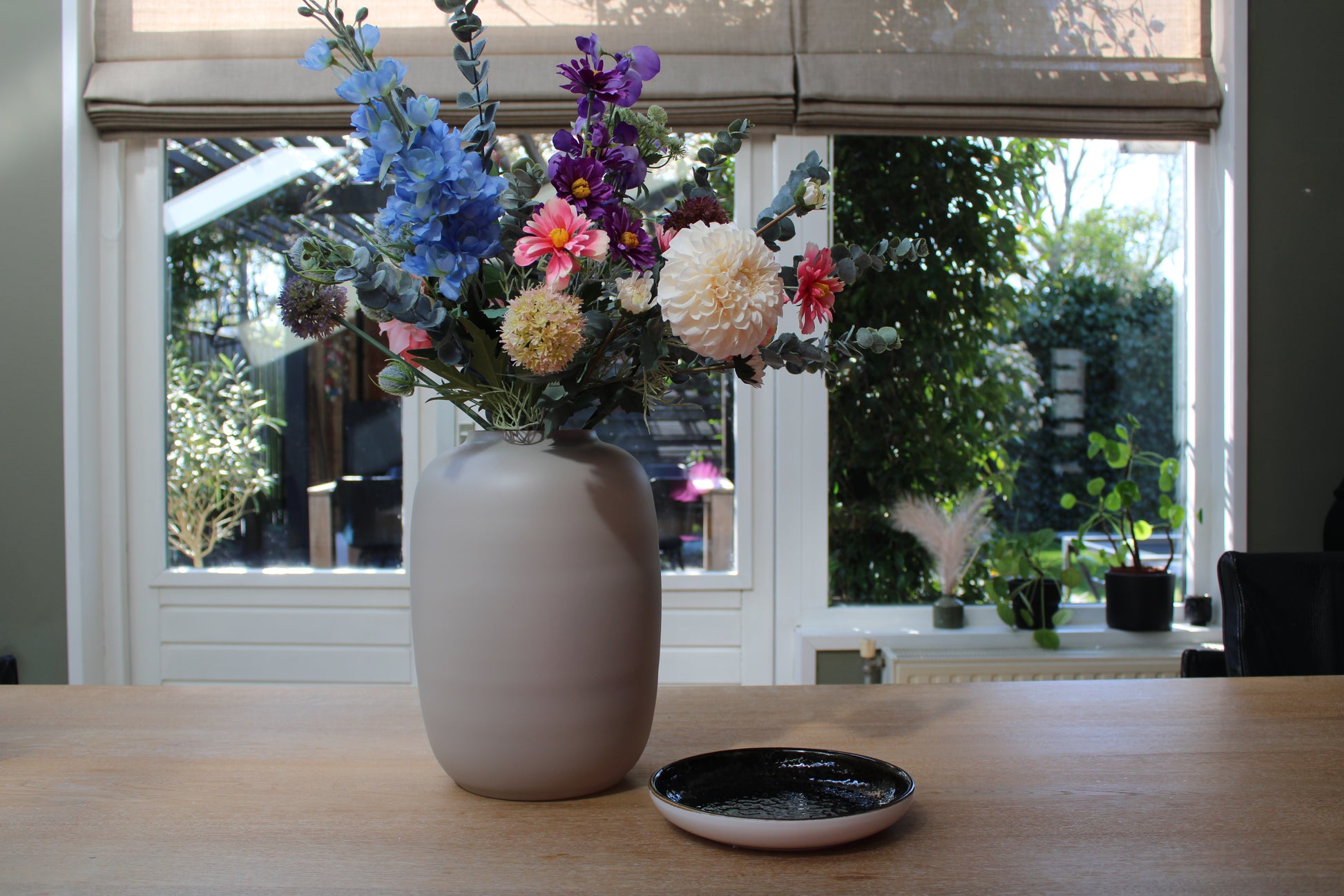 Zijden plukboeket met roze, paarse, blauwe, witte bloemen in ivoor kleurige vaas op een houten tafel
