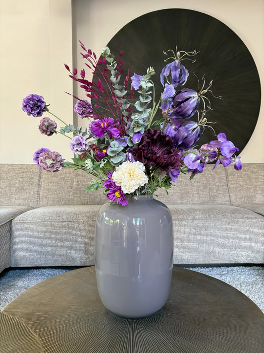 Zijden boeket Belle met paarse en lila bloemen op een tafel in een taupe kleur vaas