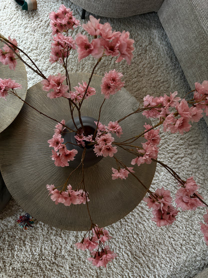 Close up: Zijden prunustak in taupe tint met verfijnde bloesems in een earth kleurige vaas van 29 cm hoog. Perfect als stijlvolle decoratie of aanvulling op een zijden boeket.